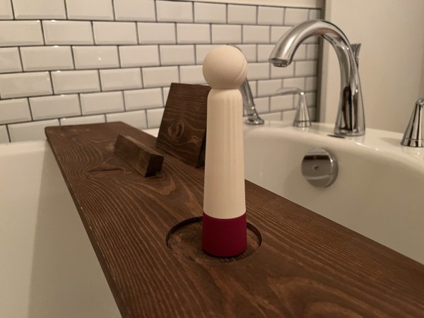 Iroha Rin vibrator stands upright on wooden bath plank across a white tub with chrome faucets in background in front of white subway tile wall