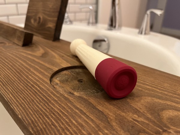 Iroha Rin vibrator lies on a wooden plank that is lying across the top of a white bathtub. There are chrome faucet handles in background